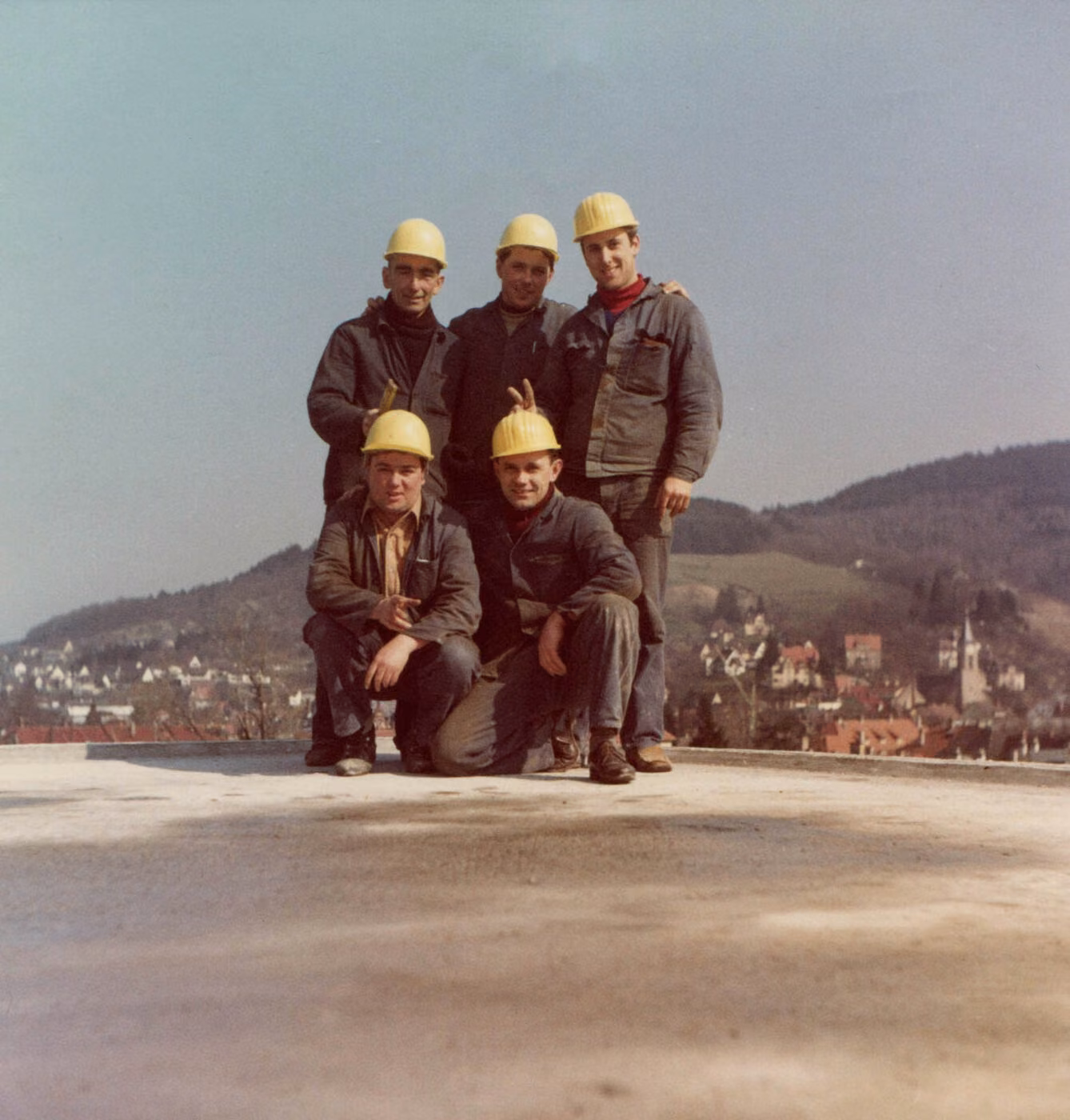 Fünf Handwerker mit Schutzhelmen posieren auf einem Flachdach mit Blick über Freiburg